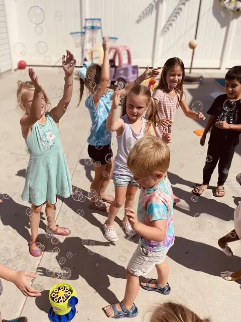 A group of kids reaching for bubbles on a sunny patio