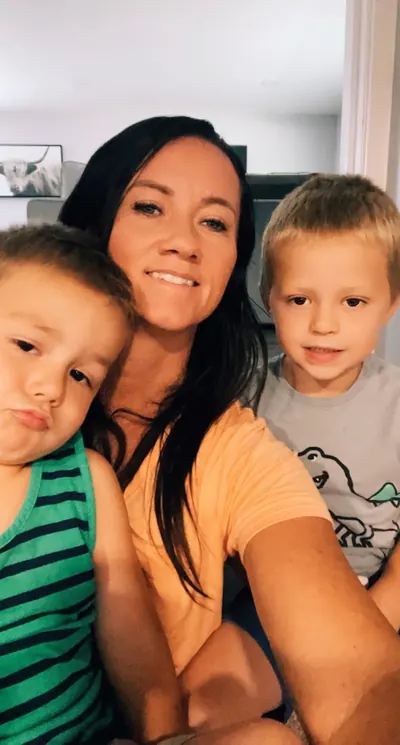 A smiling woman with long dark hair taking a selfie with two young boys