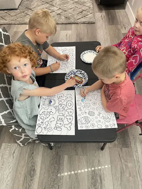 Toddlers coloring printed pages at a low black table