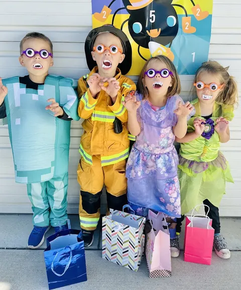 Four kids in Halloween costumes wearing silly glasses, holding treat bags