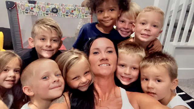 A smiling woman taking a selfie with eight grinning kids around her