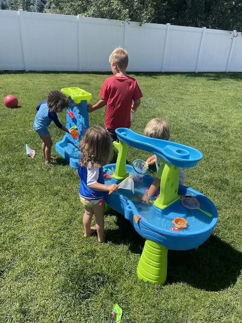 Kids playing at a blue water table on the backyard lawn